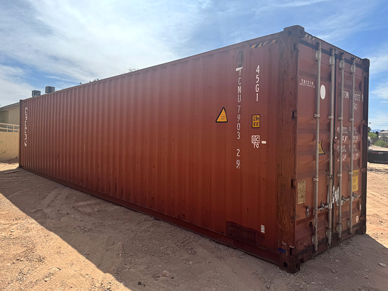 A red shipping container sitting in a dirt yard